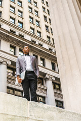 African American Businessman working in New York. Wearing gray blazer, bow tie, black pants, holding laptop computer, college student standing on street, looking up. Filtered effect..