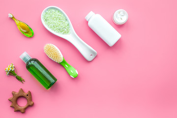 Children's means hygiene with chamomile. Bottles, spa salt, tooth brush and toy on pink background top view copyspace