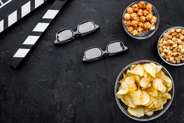 Crisp, popcorn, rusks for watching film. Clapperboard and glasses on black background top view copyspace