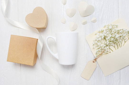 Mockup for St. Valentine's Day greeting card letter in envelope and mug wiht heart box gif, flatlay on a white wooden background, with place for your text. Flat lay, top view photo mock up