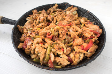 Chicken stew with red and green pepper, with red onion, pickled cucumber and spices in a frying pan.