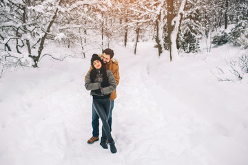 Fototapeta na wymiar Happy Young Couple in Winter . Family Outdoors. man and woman looking upwards and laughing. Love, fun, season and people - walking in winter park. It's snowing, they're hugging