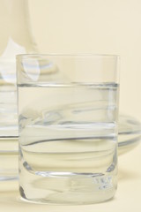 Glass and carafe with water on beige background