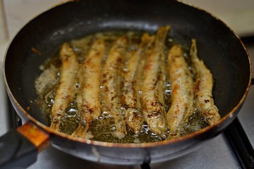 Fried smelt in a frying pan on the table with spices, lime and thyme. Small crispy fish. Selective focus