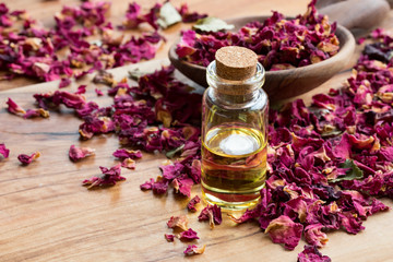 A bottle of rose essential oil with dried rose petals on a wooden table