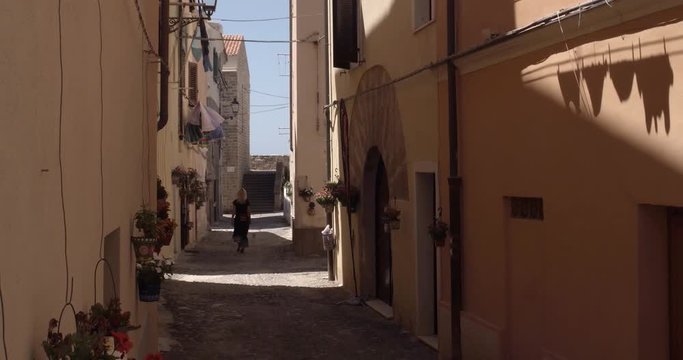 ALGHERO, SARDINIA, ITALY  &ndash; JULY 2016 : Video shot of beautiful blonde girl walking in narrow street in central Alghero on a sunny day