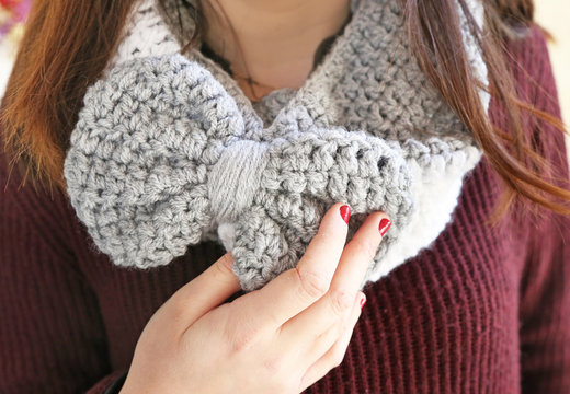woman advertises crochet grey scarf with bow - winter fashion accessories