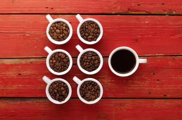 Coffee. Coffee cups and coffee beans on red wooden background.