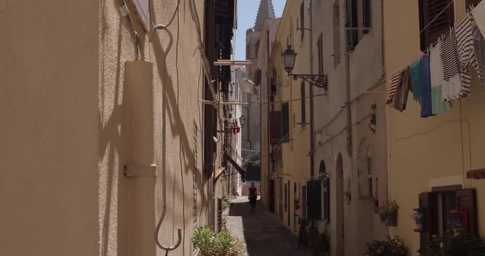 ALGHERO, SARDINIA, ITALY  &ndash; JULY 2016 : Video shot of beautiful blonde girl walking in narrow street in central Alghero on a sunny day