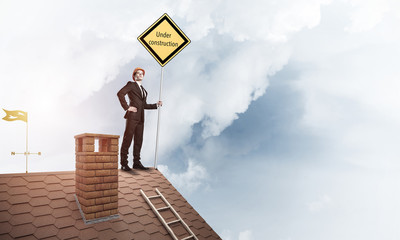 Young businessman on house brick roof holding yellow signboard. 