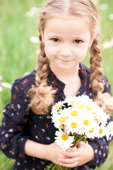 Smiling baby girl 4-5 year old holding flowers in meadow. Looking at camera. Childhood.