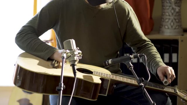 Medium tight camera slide to right of man playing slide guitar with microphones for a performance.