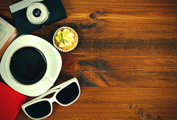 Fototapeta na wymiar Retro photo camera, coffee cup, passport, sunglasses and cupcake on brown wooden table with space for text, top view.