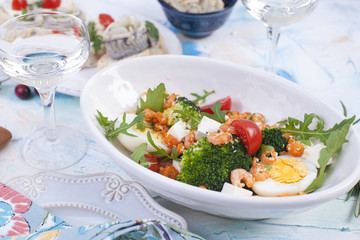 shrimp salad and vegetables in a white plate and a glass of wine, meat on a wooden board