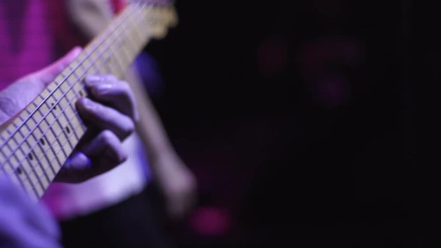 Rock musician plays solo on electric guitar on dark stage at music concert