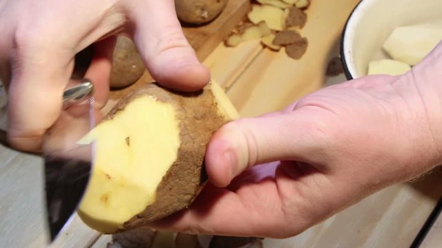 Man's hands cut potato with knife
