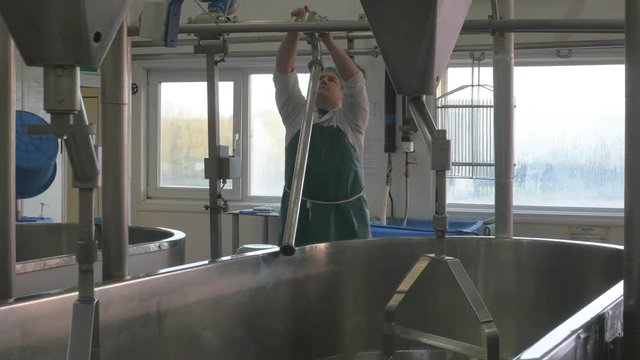 Man turning on pipe to pour milk into cheese making vat