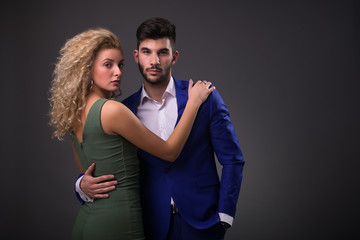 Beautiful young fashionable couple posing indoors. Beautiful blonde curly model girl in dress. Man in suit. Cute lady and handsome guy