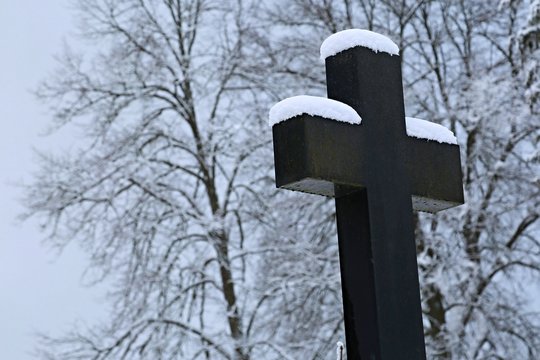 Winter scene of Christian stony cross at a cemetery and trees in the background covered with snow