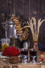 Russian traditional kettle samovar on the wooden table. Black tea, bagels, red viburnum, jam and russian samovar in the rustic style.
