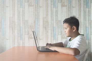 young asian boy using laptop computer at dining table at home. technology / IT concept. Computer learning concept .