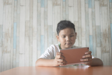 young asian boy using digital tablet at the dining table at home (focus on tablet). technology / IT concept. Computer learning concept .