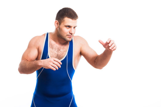 A young dark-haired man fighting wrestling, grappling in a blue wrestling tights smiles and holds his hands in fists in a fighting pose against a white isolated background