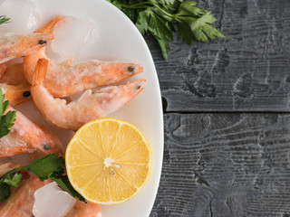 Frozen shrimp with lemon and herbs on white bowl on black wooden rustic table. Top view.