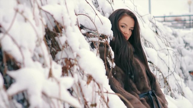 Close-up of Brunette fashionable sexy pretty rich woman or glamour model girl with beautiful long Brunette hair in waist coat of brown fur on background of Christmas tree posing for camera. slow