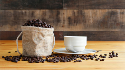 Hot coffee in a white porcelain cup with cofee bean on the wooden desk, in natural light