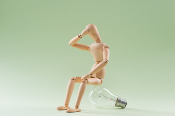 Fototapeta na wymiar Having no idea. Wood figure mannequin sitting on an incandescent light bulb