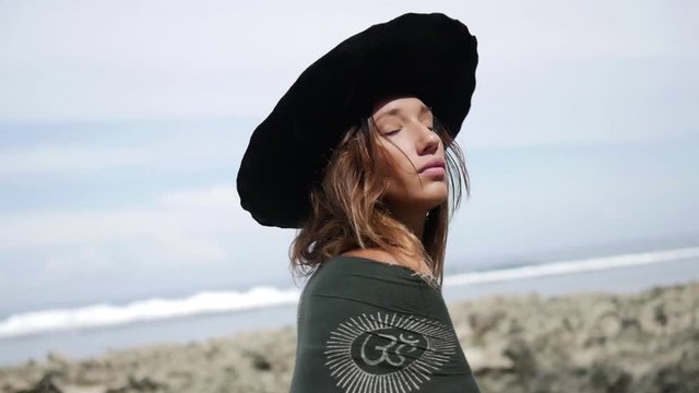 Girl in green bikini with black hat standing on the beach and wrapping in black towel