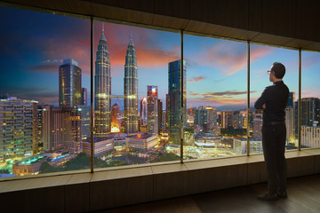 Businessman looking and thinking front of a window office with modern city skyline . Evening scene .
