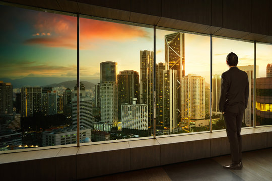 Businessman Looking And Thinking Front Of A Window Office With Modern City Skyline . Sunrise Scene .