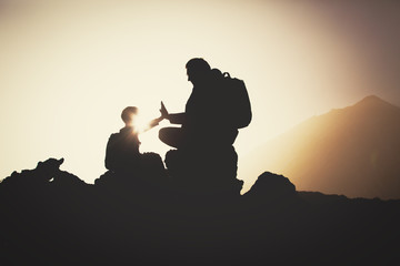 Silhouettes of father and son hiking in mountains at sunset