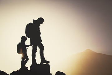 Silhouettes of father and son hiking in mountains at sunset