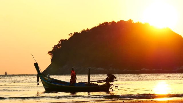 Silhouette long tail boat converted to boat excursions and  tourist floating in the andaman sea with golden light of the Sun and island background in travel or transportation concept.