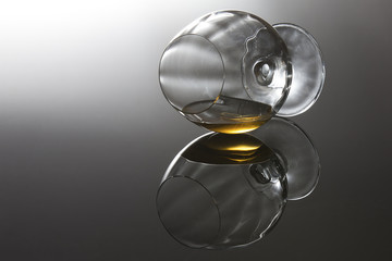 Brandy in a cognac glass lying on its side on shiny surface with reflection