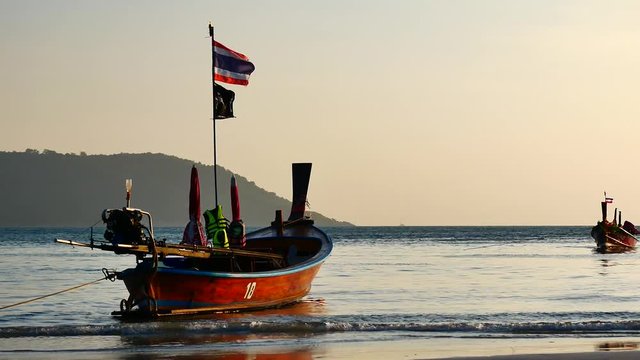 Travel Video long tail boat converted to boat excursions on the bech at andaman sea with golden light of the Sun  before sunset in travel or transportation concept.