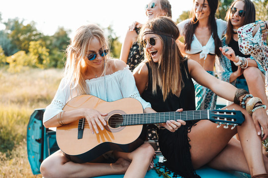 Girls are sitting on the trunk with a guitar