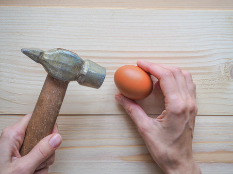 Hand, hammer and egg on wooden background. The concept of complex problems, the challenge can be solved.
