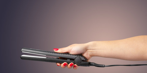 Woman hand with a hair iron isolated on a color background