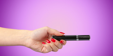 Woman hand with mascara cosmetic tube isolated on color background