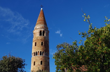 The cylindrical shape topped by conical cusp bell tower made by red bricks in the venetian village of Caorle in Veneto, Italy

