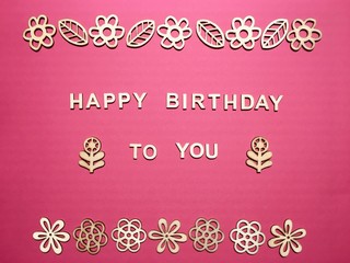 Fototapeta na wymiar Happy birthday to you made of wooden letters with a wooden floral frame on a pink background