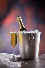 Champagne bottle in bucket with ice and glasses of champagne on dark background