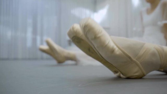 Closeup of foot in ballet pointes do training and stretching muscles. Two pairs of female feet on floor knead feet before performing in ballet.
