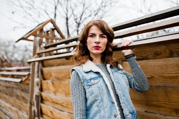 Portrait of brunette curly girl in jeans jacket against wooden wall.