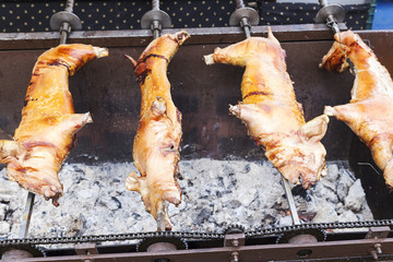 three pork skewered on an iron cooking on some embers in a market on the street
