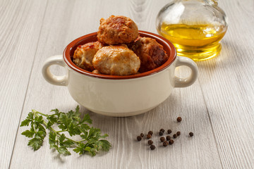 Fried meat cutlets in ceramic soup bowl, glass bottle with sunflower oil, branch of fresh parsley and black peppercorn